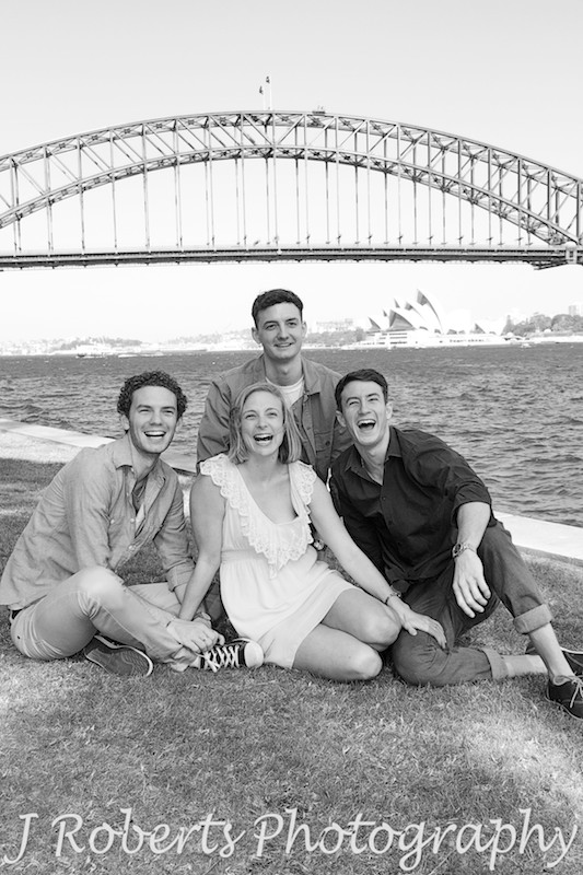 laughing siblings sitting on grass with harbour views in background - Family Portrait Photography Sydney
